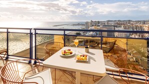 A balcony with a table set for two, featuring a plate of fruit and a glass of orange juice. The balcony overlooks a beach and cityscape. - Hotel Yaramar - Adults Recommended (Fuengirola)