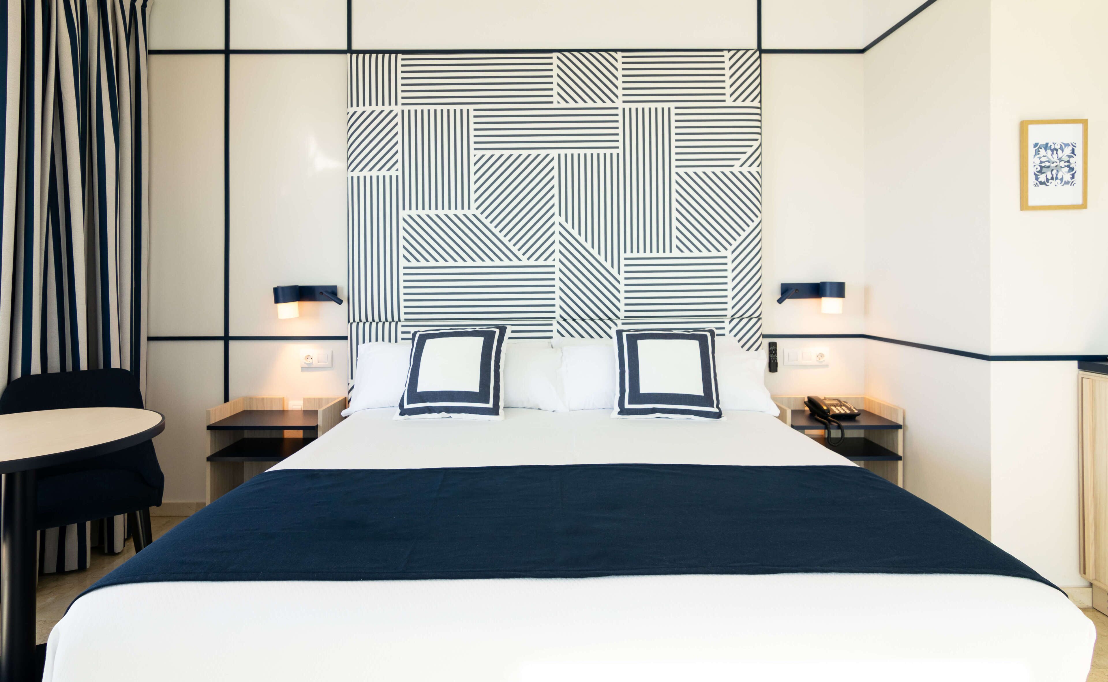 Une chambre d’hôtel avec un grand lit, deux tables de chevet, une chaise et une tête de lit à motifs.