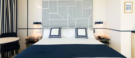 A hotel room with a large bed, two bedside tables, a chair, and a patterned headboard.