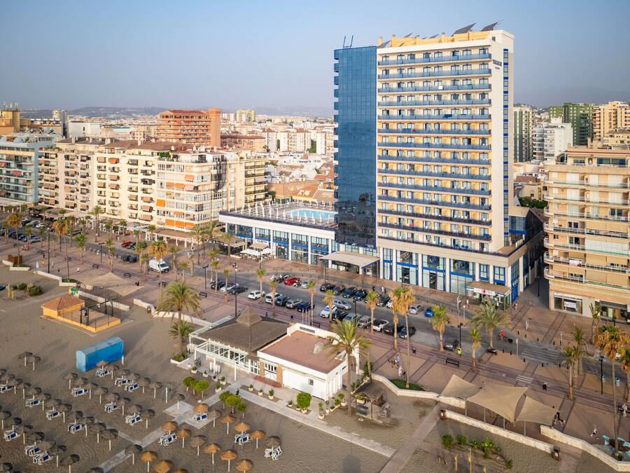A high-rise hotel with multiple floors, a swimming pool, and a parking area with umbrellas.