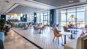 A spacious hotel lobby with multiple seating areas, large windows offering a view of the beach, and a bar area with shelves of bottles. - Hotel Yaramar - Adults Recommended (Fuengirola)