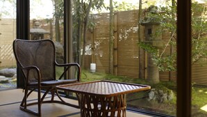 A room with a wicker chair and a woven table, large windows, and a view of a bamboo fence and greenery outside. - Kinjohro Kanazawa (Kanazawa)