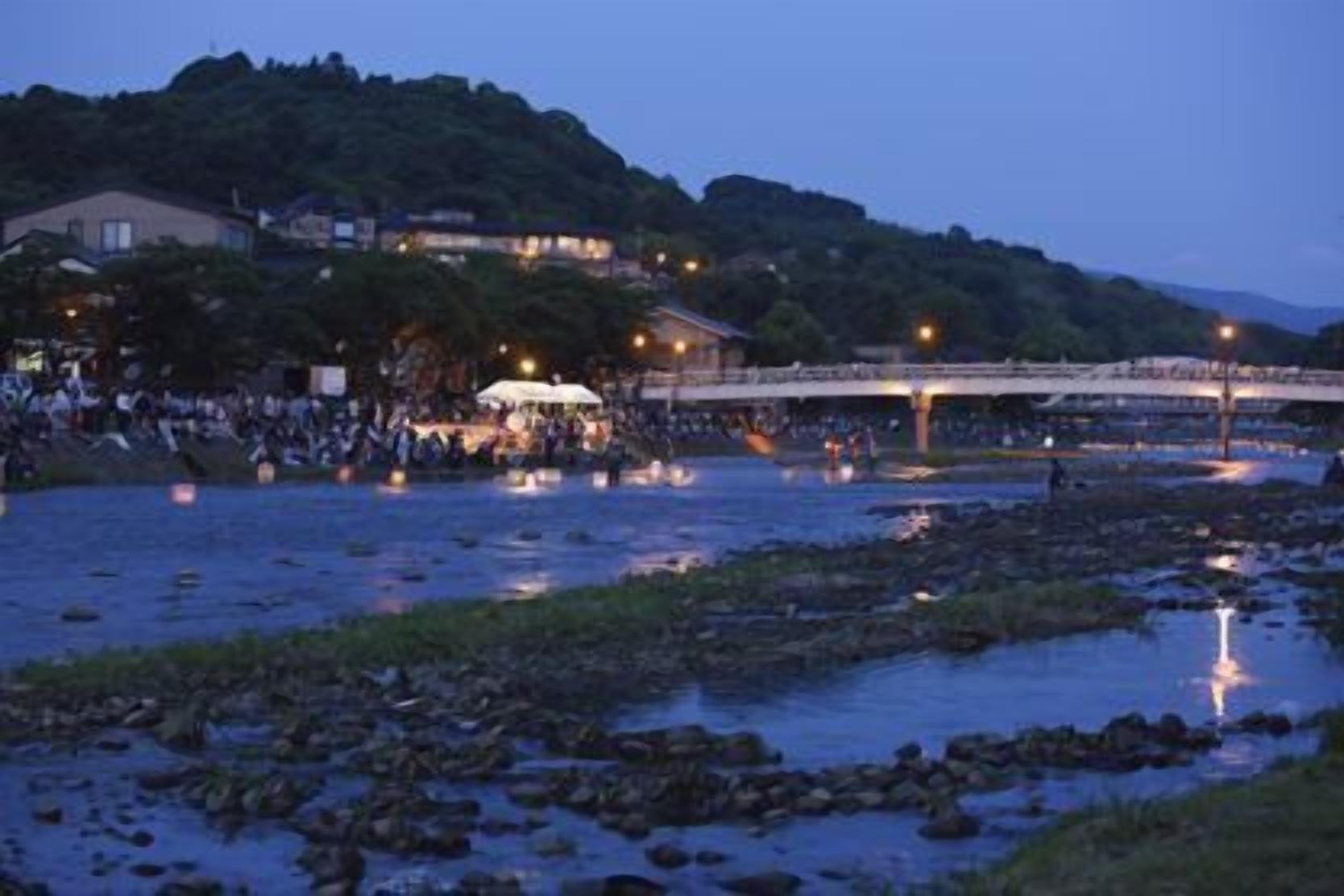 A riverside area with a bridge, buildings, and a crowd of people.