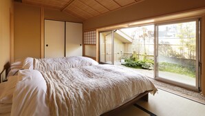 A traditional Japanese-style bedroom with tatami flooring, a large bed with white bedding, sliding doors, and a view of a garden through a sliding glass door. - Kinjohro Kanazawa (Kanazawa)