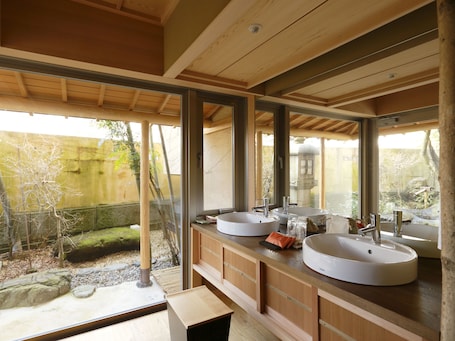 A modern bathroom with two large sinks, wooden cabinetry, and large windows offering a view of a garden.