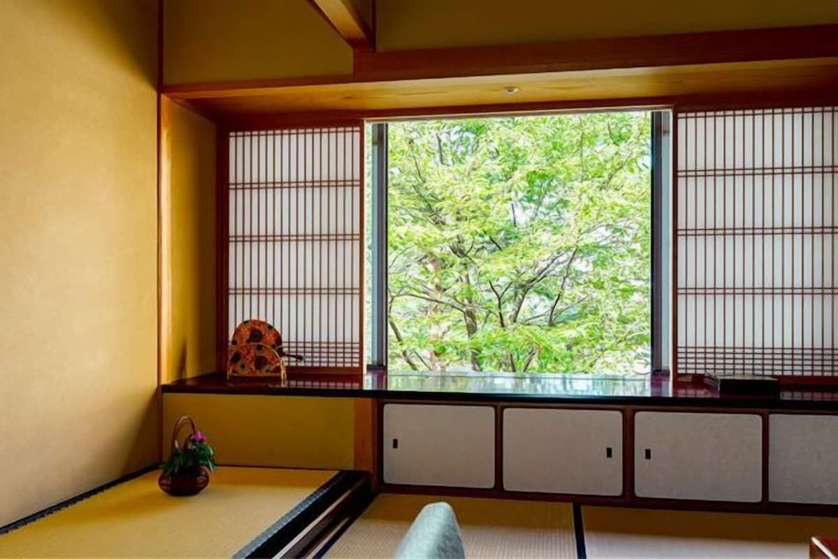 Une pièce de style japonais traditionnel, avec un sol recouvert de tatamis, une petite table en bois et une fenêtre ornée de stores en bambou.