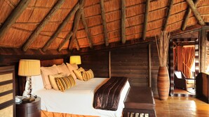 A wooden cabin room with a bed, bedside lamps, a large vase, and a wooden bench.