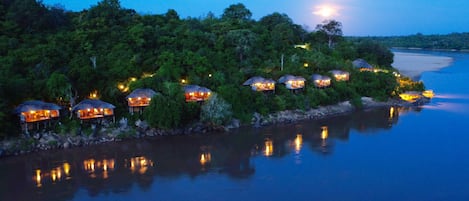 A series of thatched-roof huts along a riverside, surrounded by dense greenery.