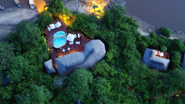 An aerial view of a resort with a swimming pool, lounge area, and boats on the shore.