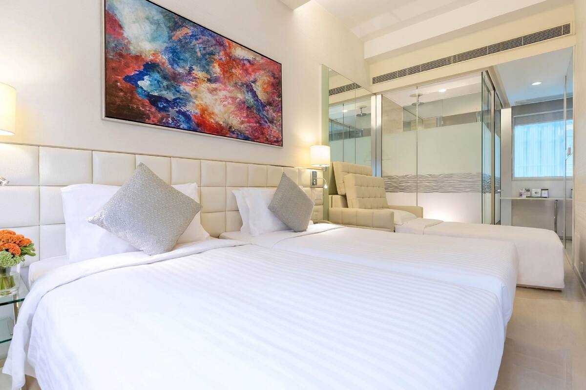 Ein modernes Hotelzimmer mit einem großen Bett, einer Couch, einer Glaskabinent Dusche und einem farbenfrohen abstrakten Gemälde an der Wand.