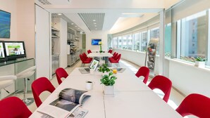 Une salle de conférence moderne équipée d’une longue table, de chaises rouges, d’un tableau blanc et d’un écran de télévision.