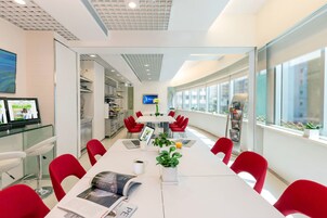 A modern conference room with a long table, red chairs, a whiteboard, and a TV screen.