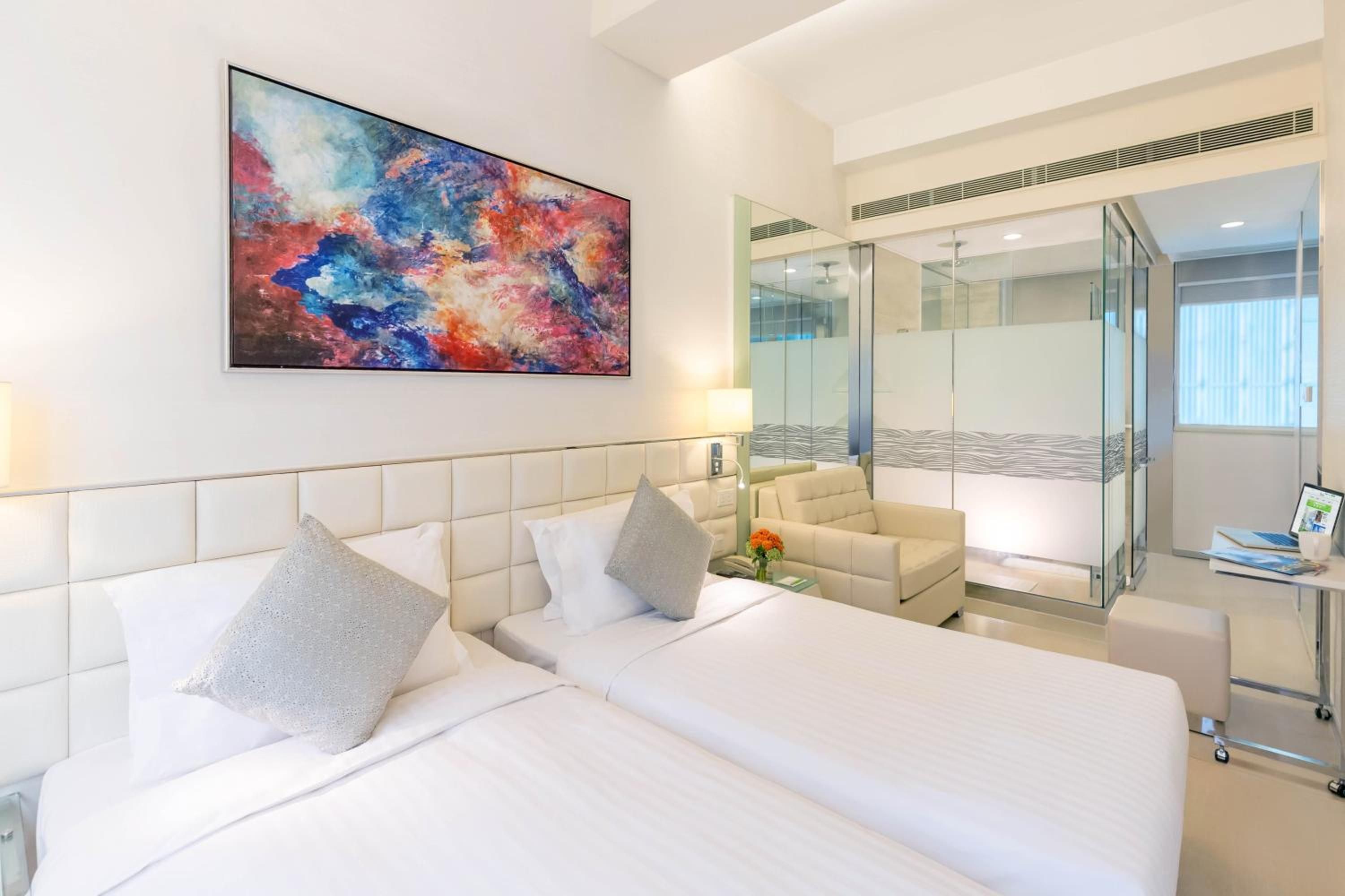 Une chambre d’hôtel avec deux lits, une grande peinture abstraite, une douche en verre et un ordinateur portable posé sur un bureau.