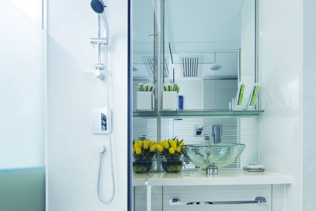 Ein modernes Badezimmer mit Duschkabine aus Glas, einem weißen Waschtisch mit Spiegel und einer Glasvase mit gelben Blumen.