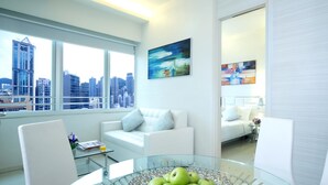 Un salon moderne avec une table basse en verre, des canapés blancs et une vue sur la ville grâce à de grandes fenêtres.
