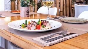 A dining table with a plate of food, a glass of white wine, and a vase with green plants. - Hotel Melilla Puerto (Melilla)