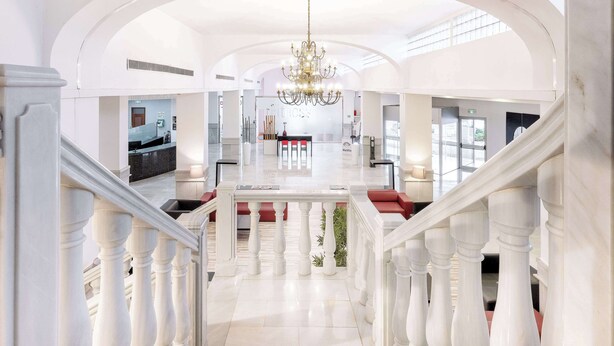 A spacious lobby with a grand staircase, a chandelier, and a reception desk. - Hotel Melilla Puerto (Melilla)