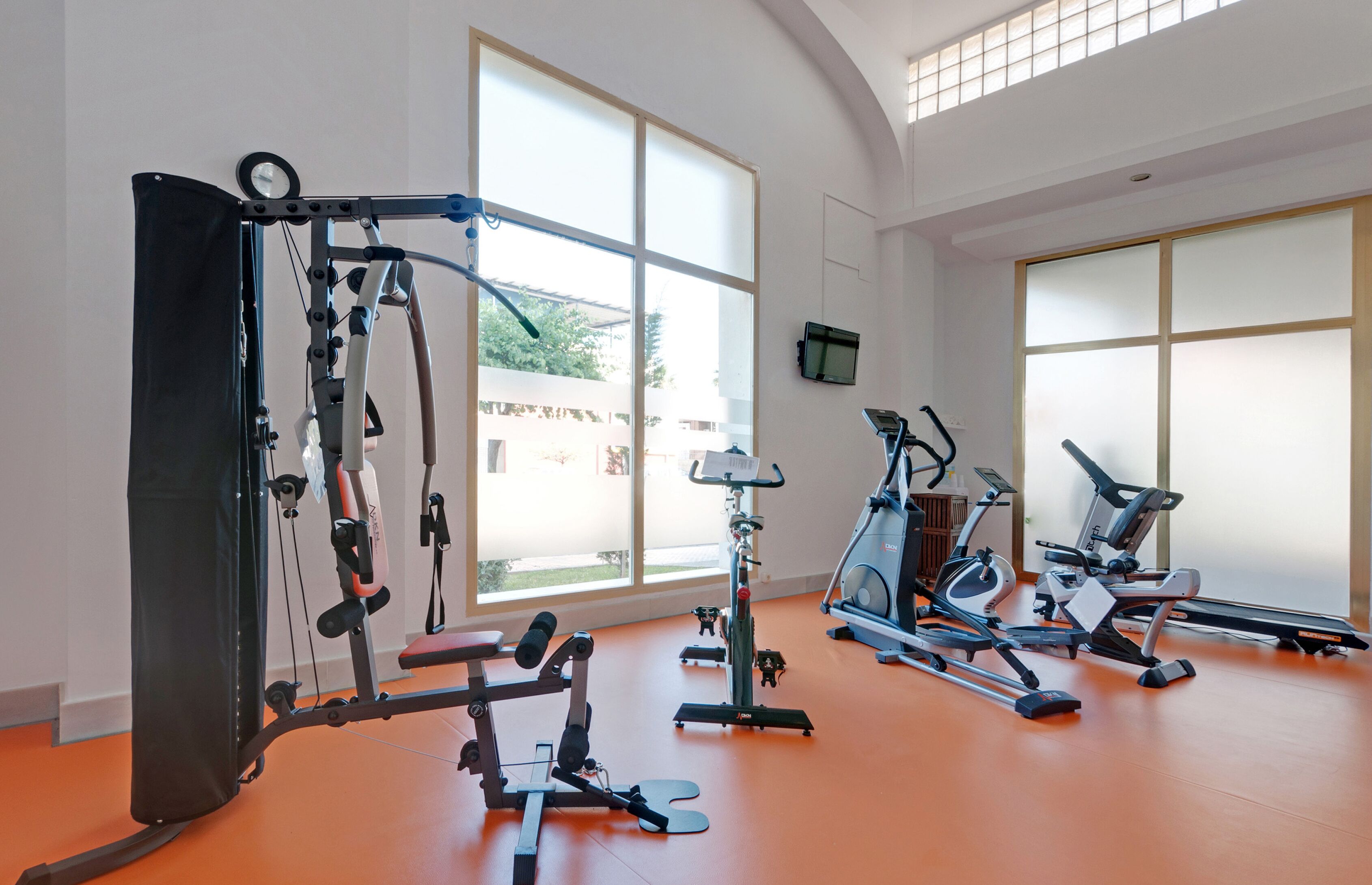 A gym with various exercise equipment, large windows, and a view of the outside.