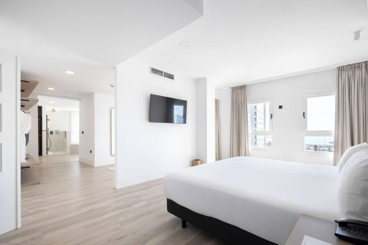Ett modernt hotellrum med en stor säng, en platt-TV som är monterad på väggen och utsikt över staden genom fönstret.