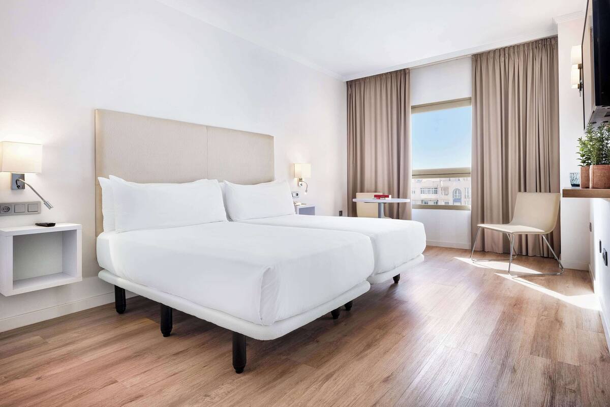 Ett hotellrum med en stor säng, ett skrivbord, en stol och utsikt över staden.