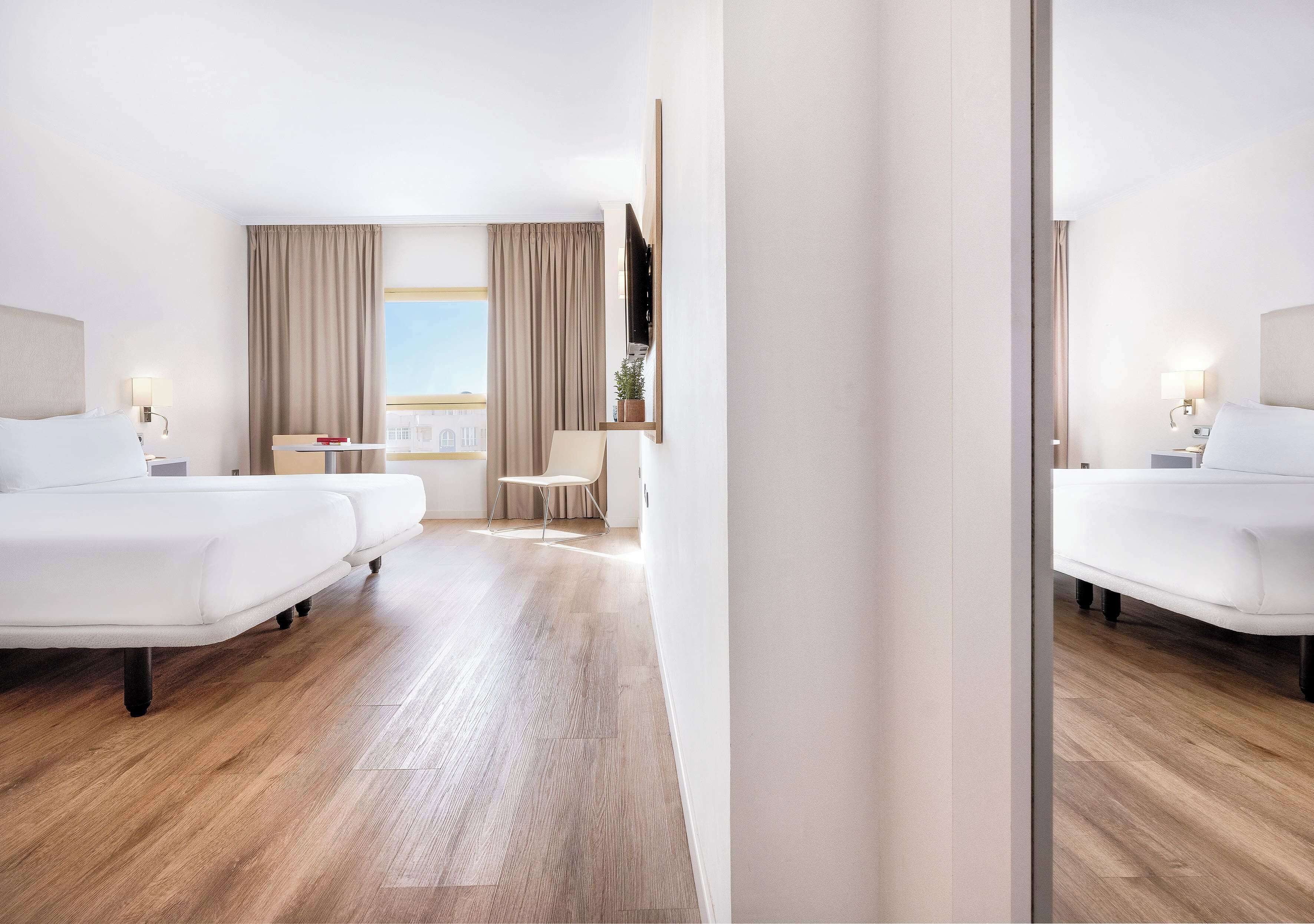 A hotel room with a large bed, a desk, a chair, and a window with curtains.