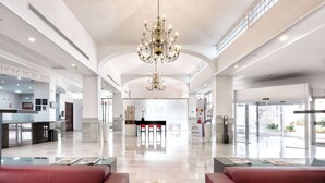 A spacious lobby with a chandelier, red seating, a reception desk, and a glass wall with a 'Melinda' sign. - Hotel Melilla Puerto (Melilla)