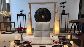 Una habitación con una zona de estar central, un tapiz circular y varios cuencos y velas dispuestas sobre una mesa blanca.