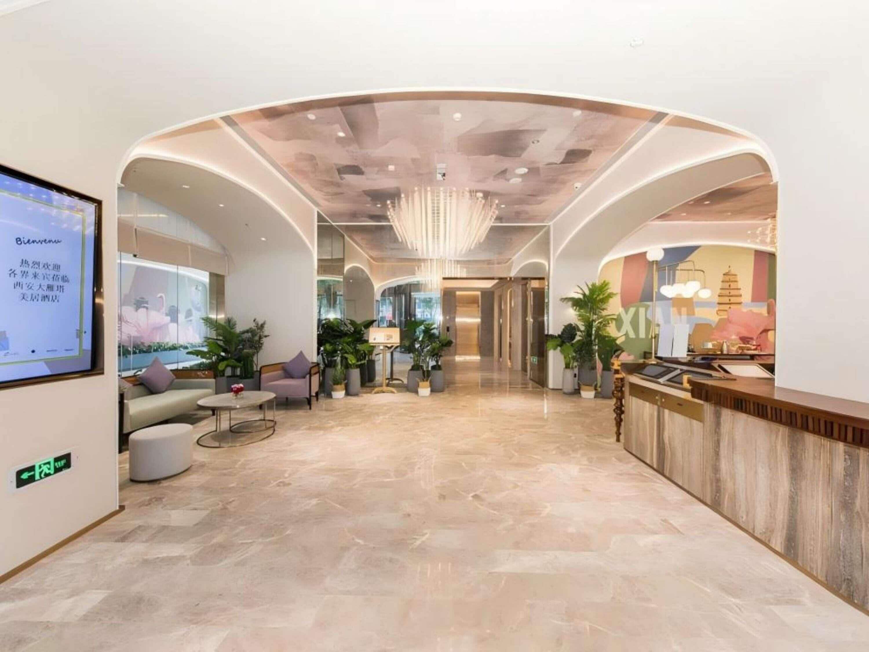 Un moderno vestíbulo de hotel con mostrador de recepción, zona de estar y una gran pantalla digital que muestra información.