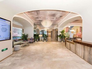 A modern hotel lobby with a reception desk, seating area, and a large digital screen displaying information.