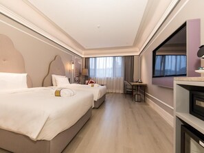 Hotellihuone, jossa on kaksi sänkyä, työpöytä, tuoli, televisio ja ikkuna, jossa on verhot.