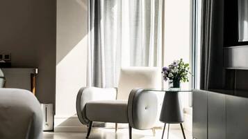 Une chambre d’hôtel moderne dotée d’une grande fenêtre, d’un fauteuil blanc, d’une table basse en verre et d’un téléviseur à écran plat.