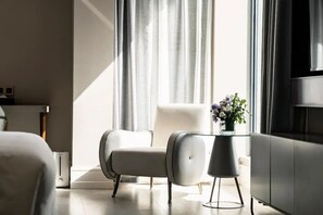 Une chambre d’hôtel moderne dotée d’une grande fenêtre, d’un fauteuil blanc, d’une table basse en verre et d’un téléviseur à écran plat.