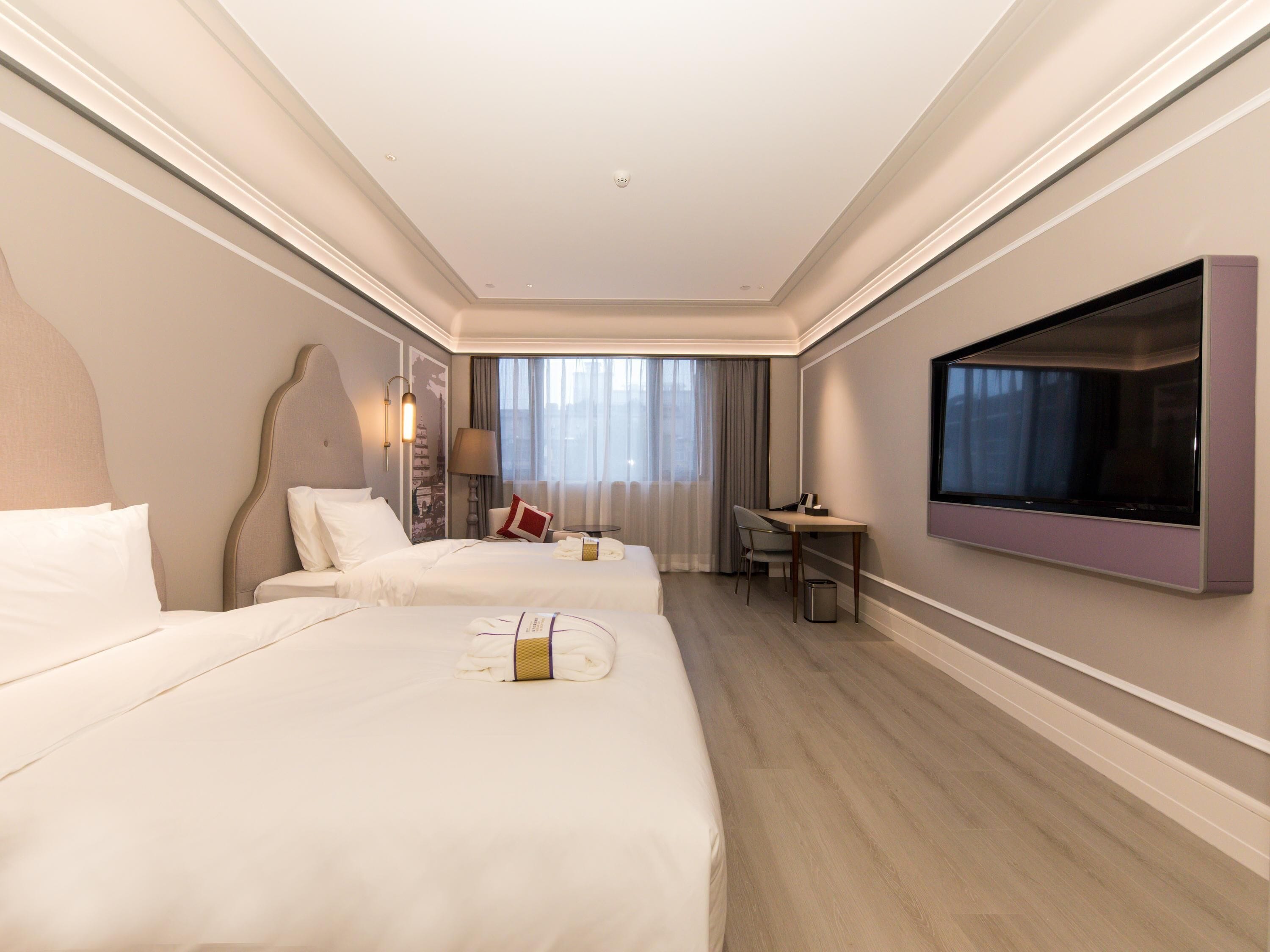 A hotel room with two beds, a desk, a TV, and a window with curtains.
