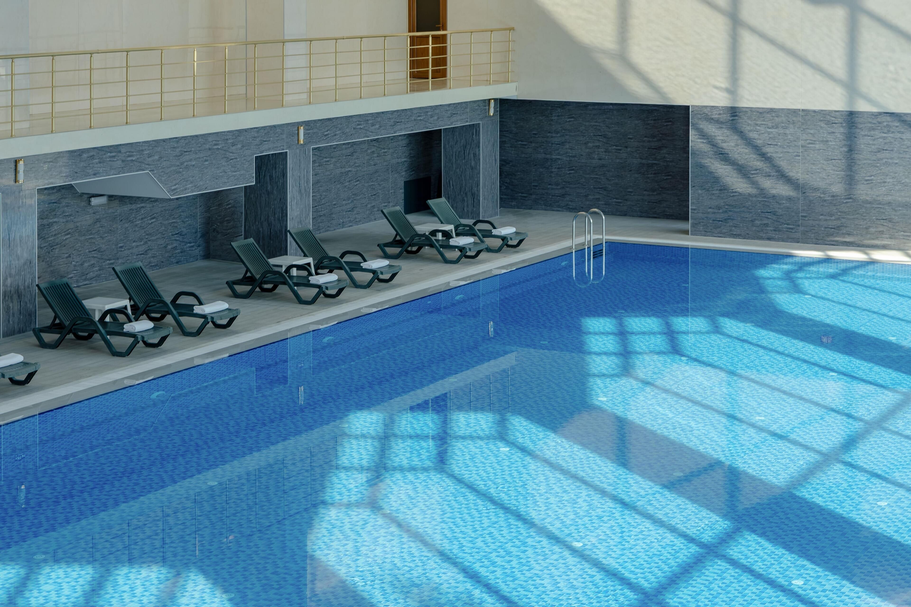Una piscina interior con numerosas tumbonas y una superficie de agua azul cristalina.
