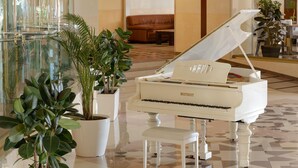 Un grand piano dans un hall d’entrée, agrémenté de plantes en pot, avec un canapé en cuir marron en arrière-plan.