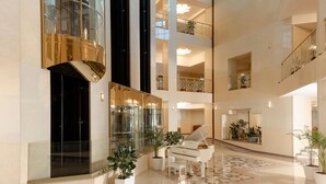 Un hall d’entrée spacieux avec un grand piano, de nombreux étages et des plantes en pot.