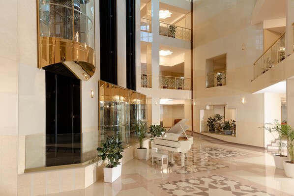 Un hall d’entrée spacieux avec un grand piano, de nombreux étages et des plantes en pot.