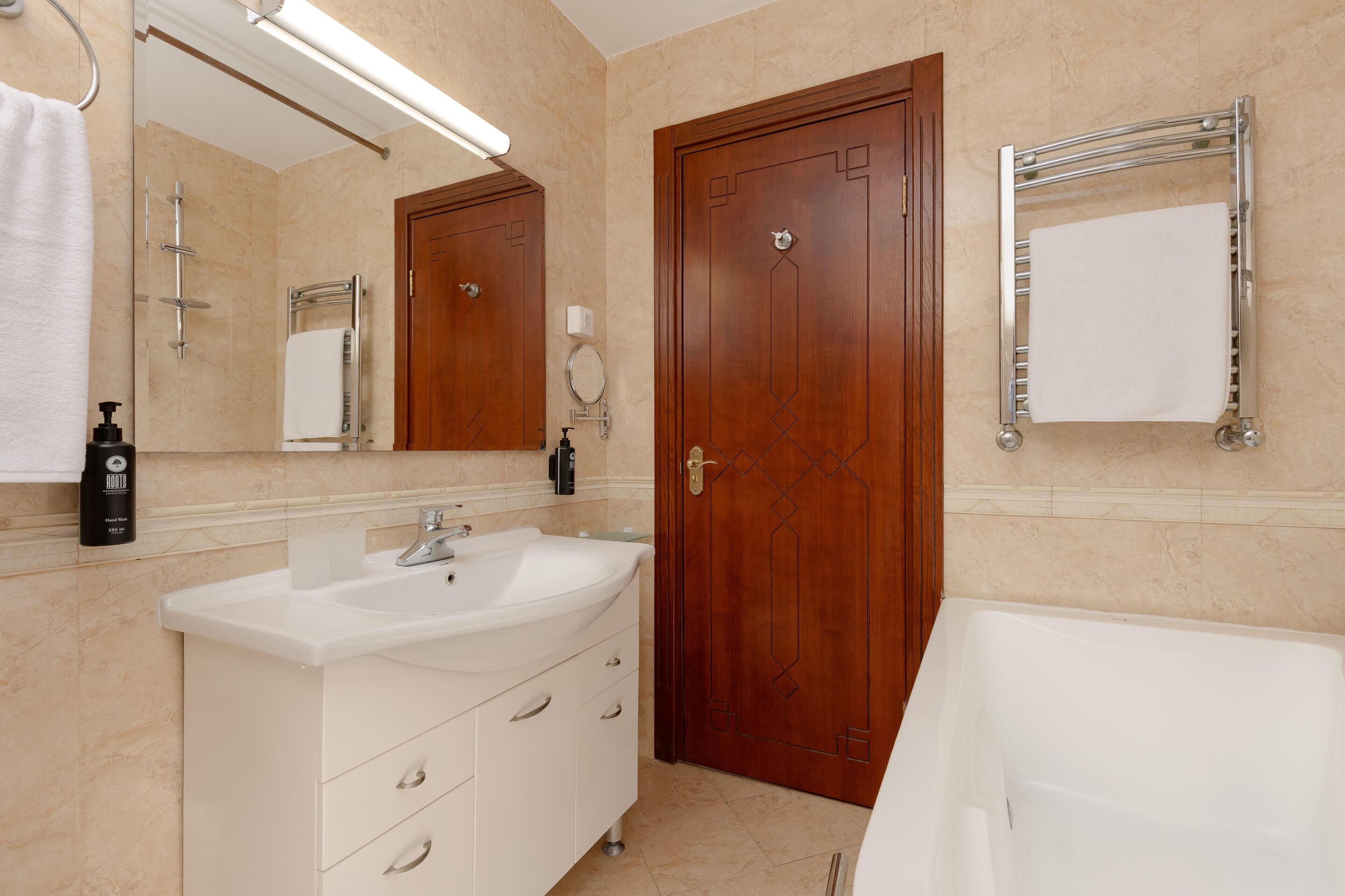 A bathroom with a white sink, a mirror, a wooden door, and a towel rack.