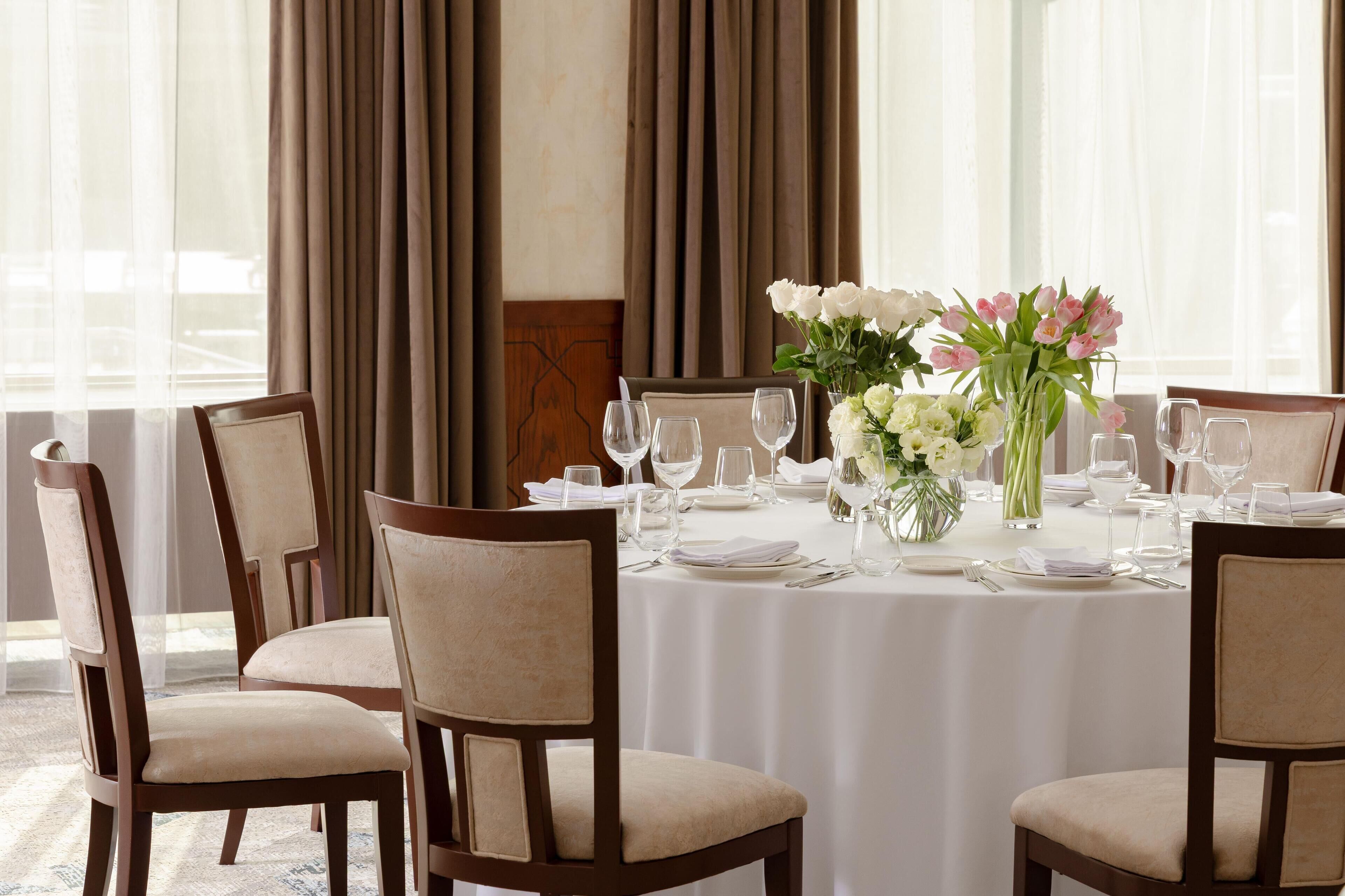 A dining table set for four with white tablecloth, chairs, and a vase of flowers.