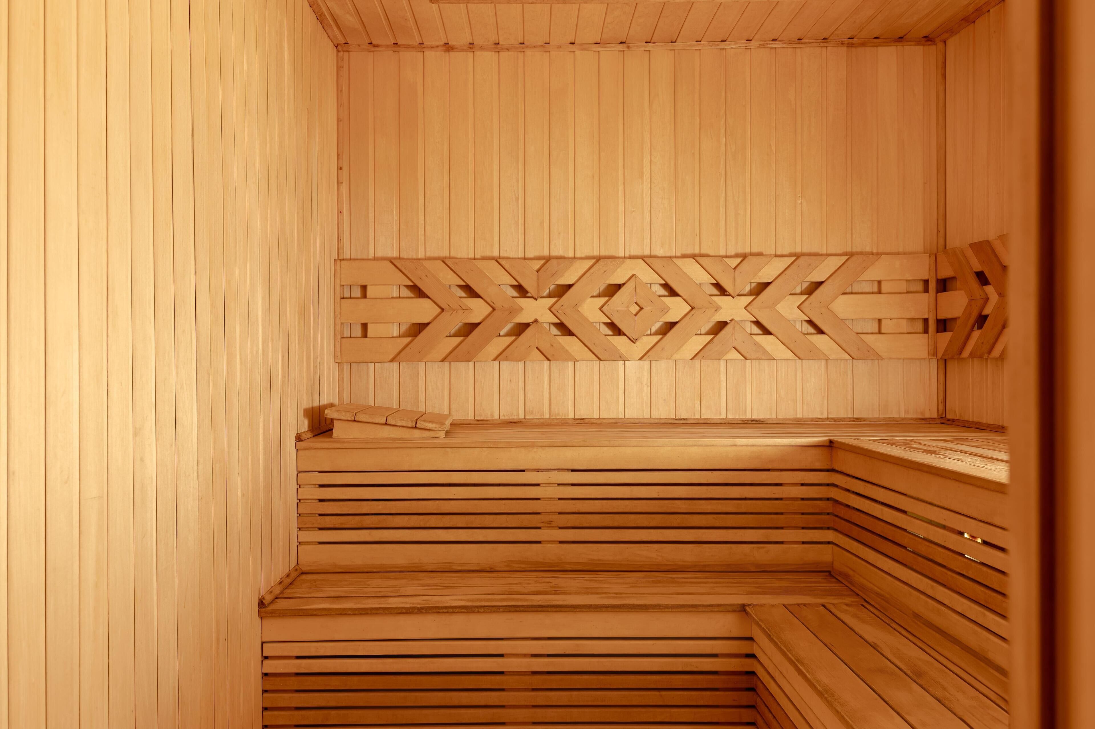 A wooden sauna with a geometric patterned wall, tiered seating, and a bench.