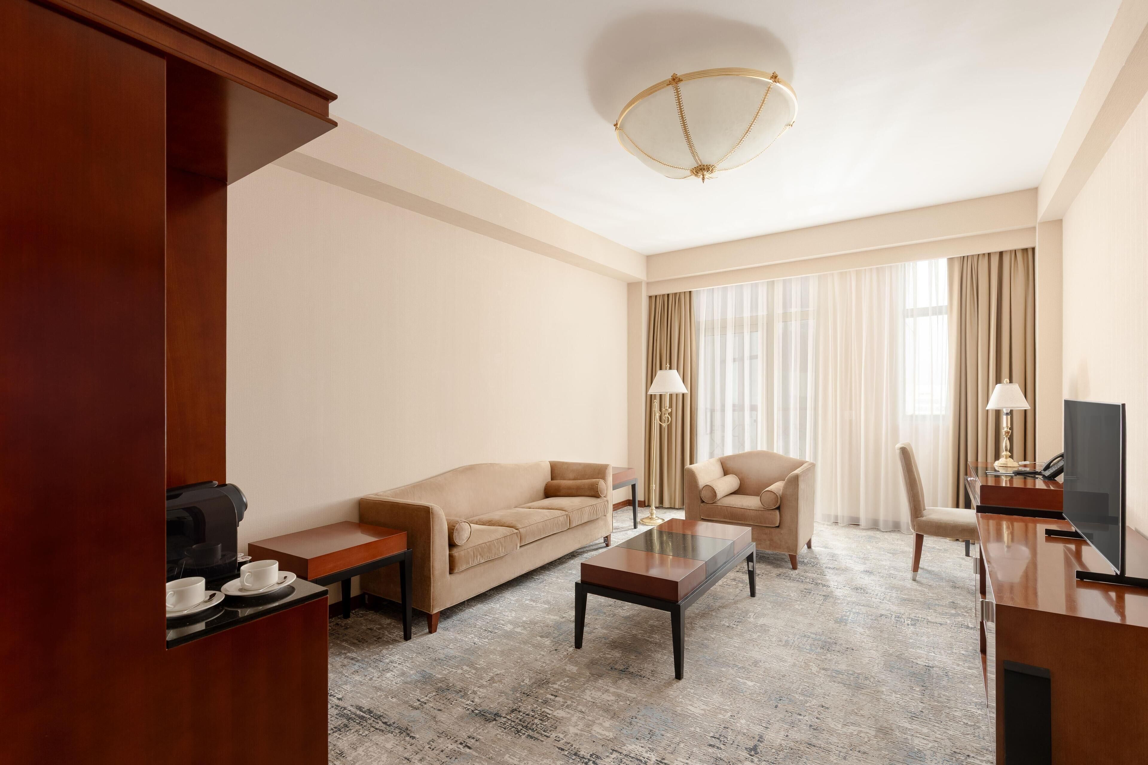 A hotel room with a sofa, armchair, coffee table, TV, and a coffee machine.