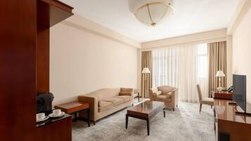 A hotel room with a sofa, armchair, coffee table, TV, and a coffee machine.