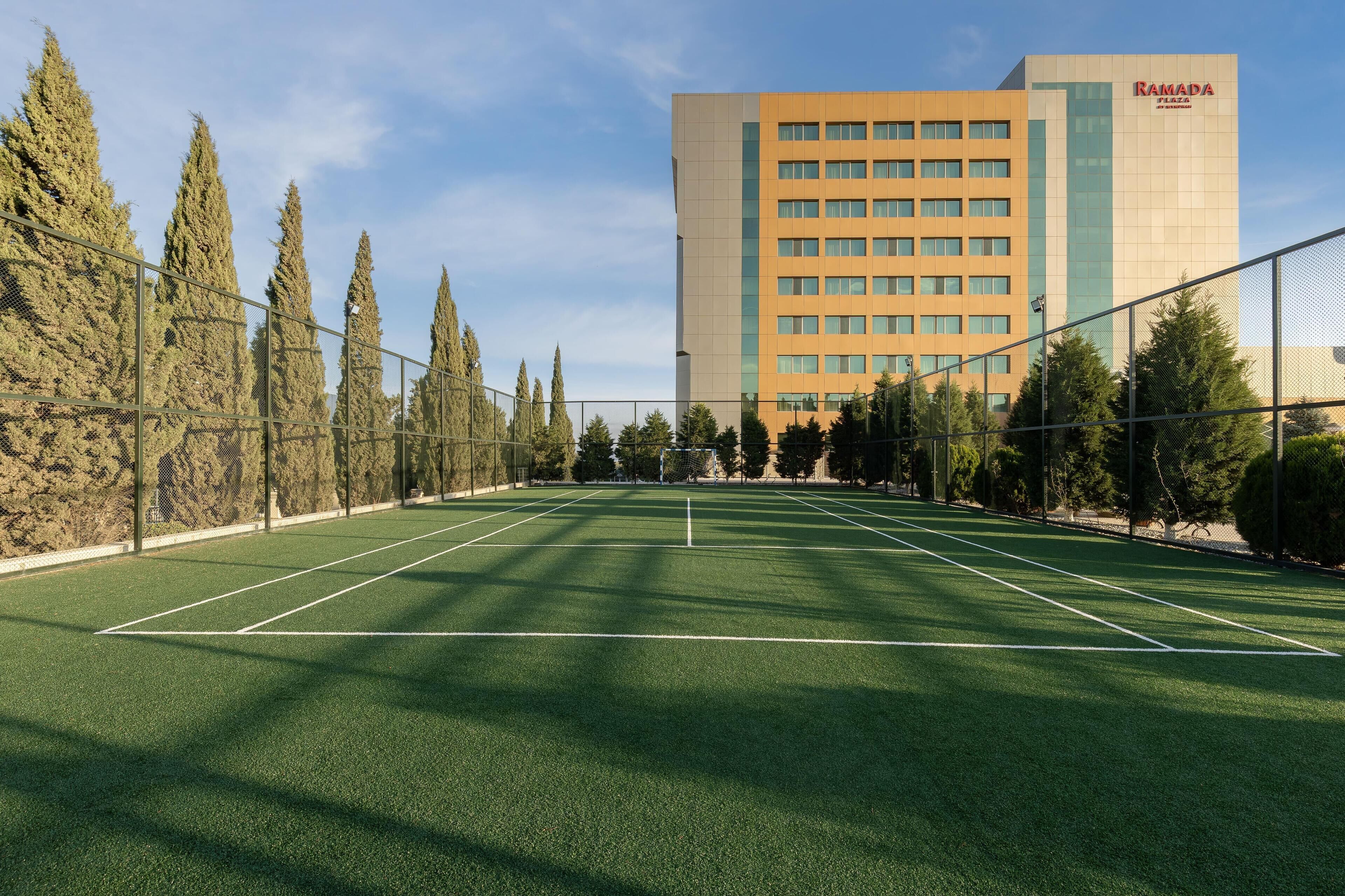 A tennis court with a Ramada hotel in the background.