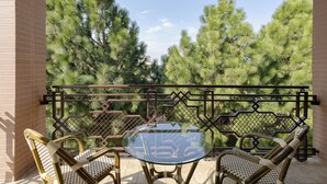 Un balcon avec une table en verre et deux fauteuils en osier, donnant sur une zone boisée.