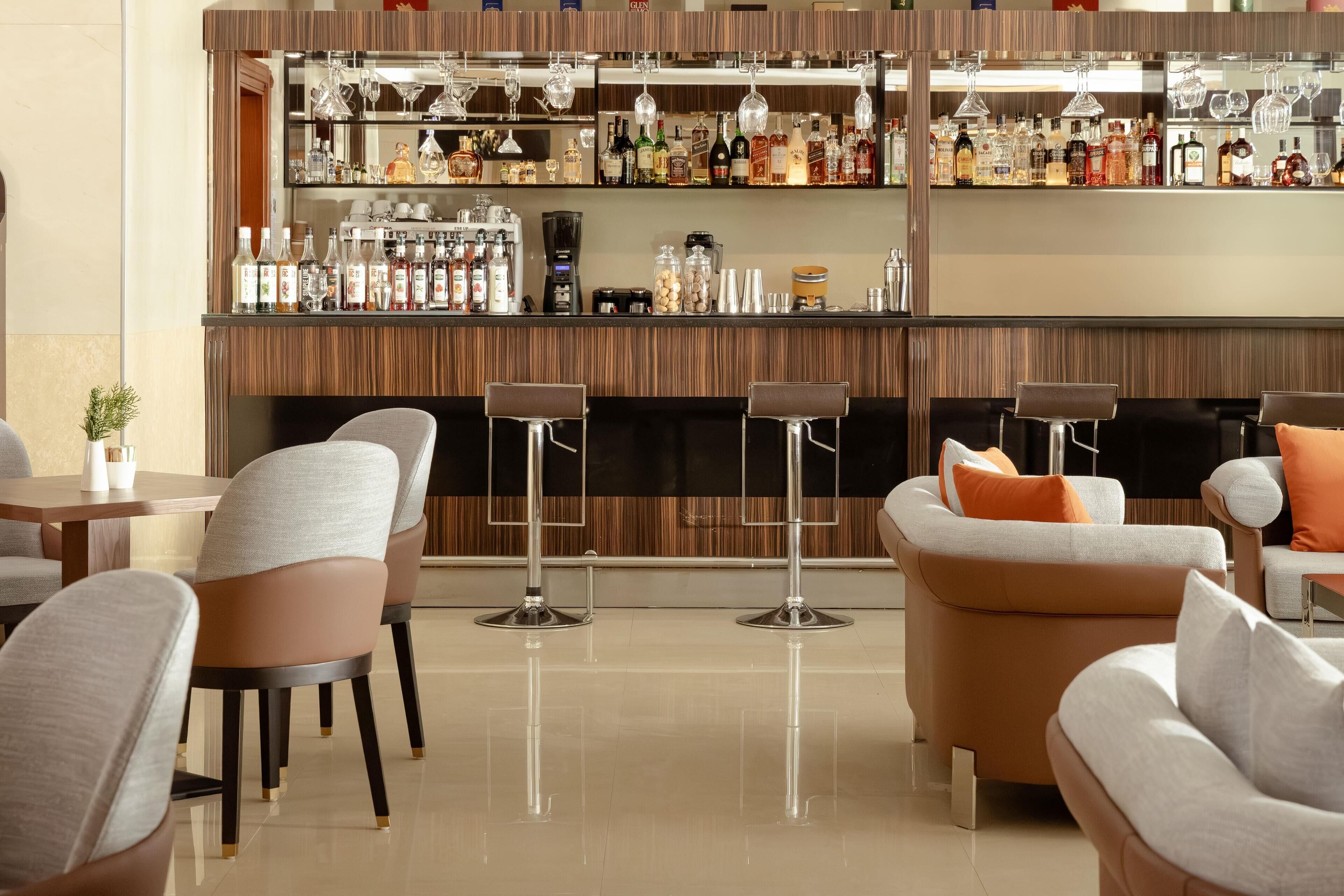 Un espace bar doté de plusieurs étagères remplies de bouteilles d’alcool et de verres, de tabourets de bar et d’un coin salon avec des fauteuils confortables.