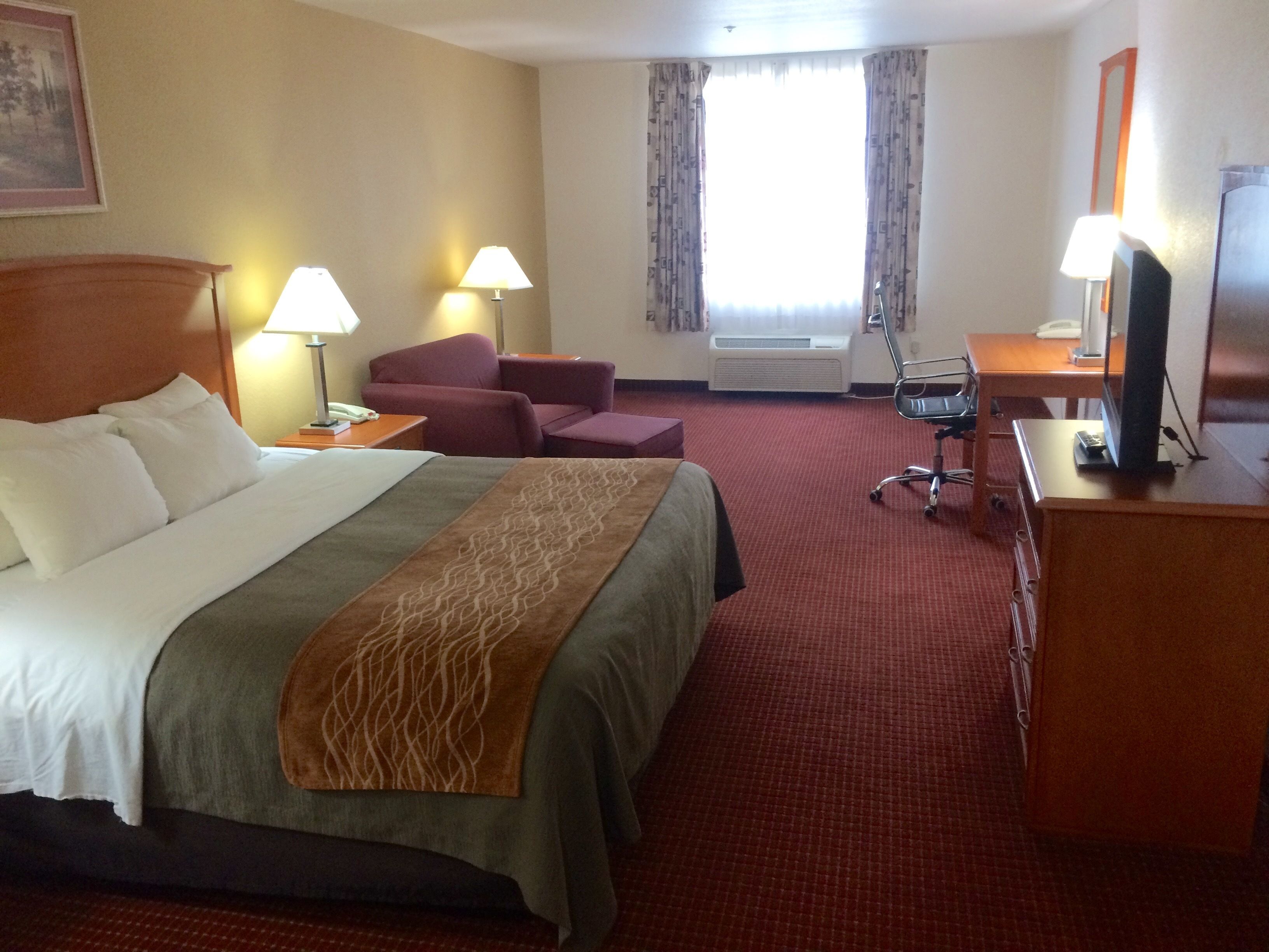Habitación de hotel con cama, escritorio, silla, televisor y ventana con cortinas.