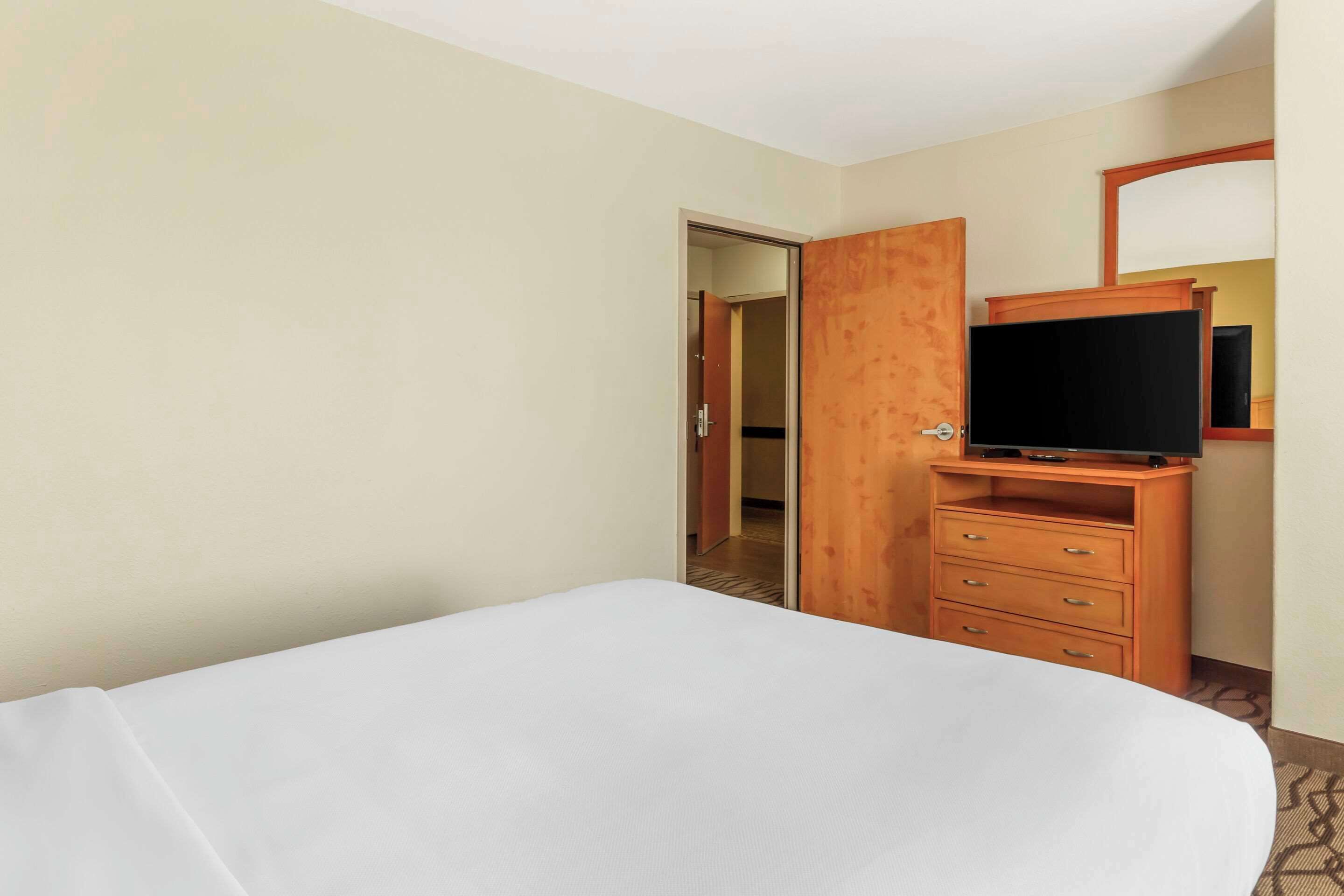 A hotel room with a bed, a wooden dresser with a television, and a door leading to another room.