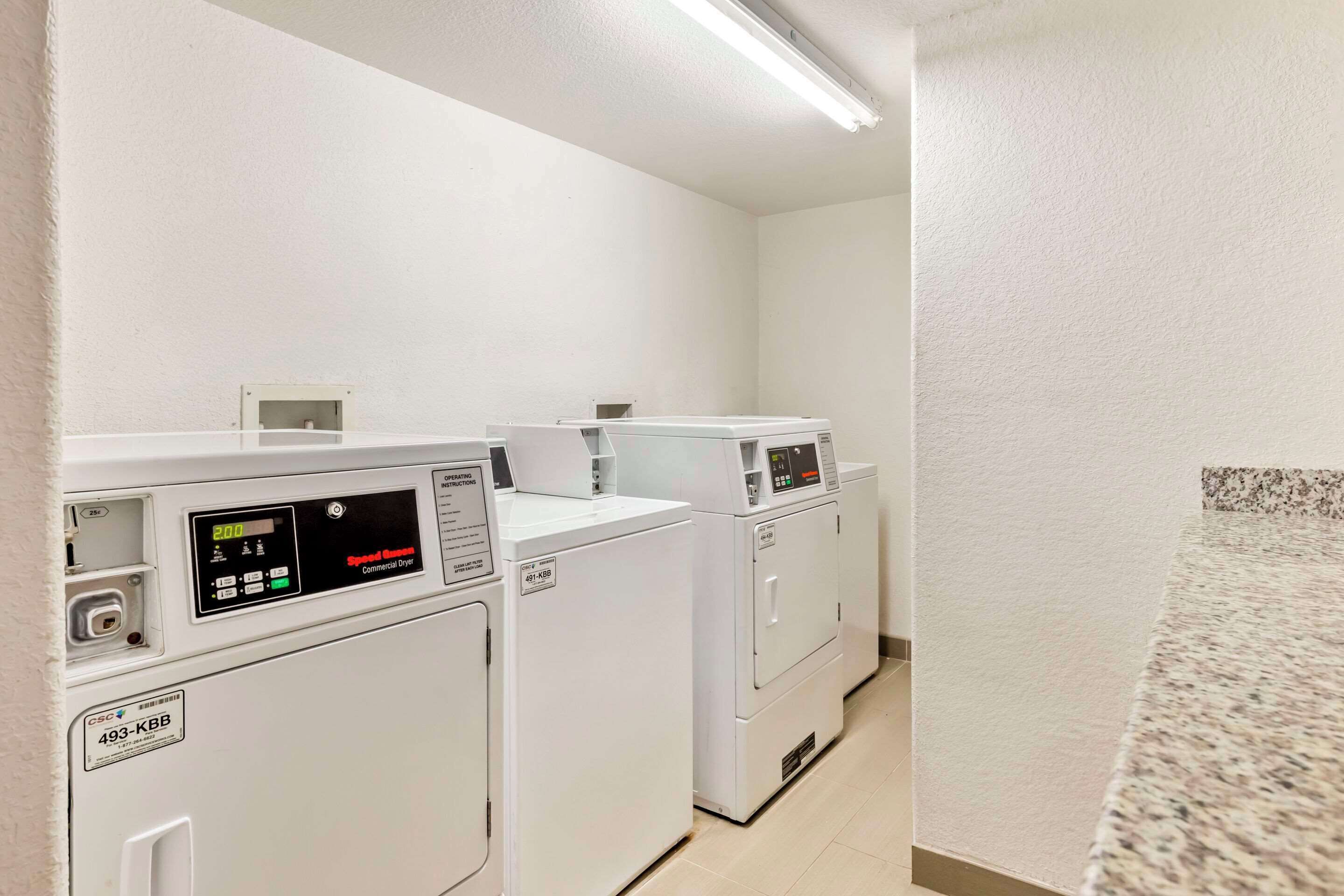 A laundry room with commercial dryers and a control panel.
