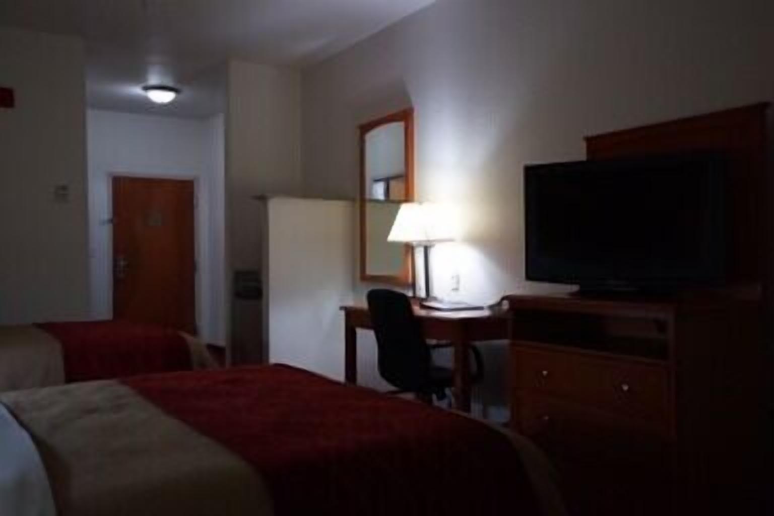 Une chambre d’hôtel avec deux lits, un bureau, une chaise, une télévision et une lampe.