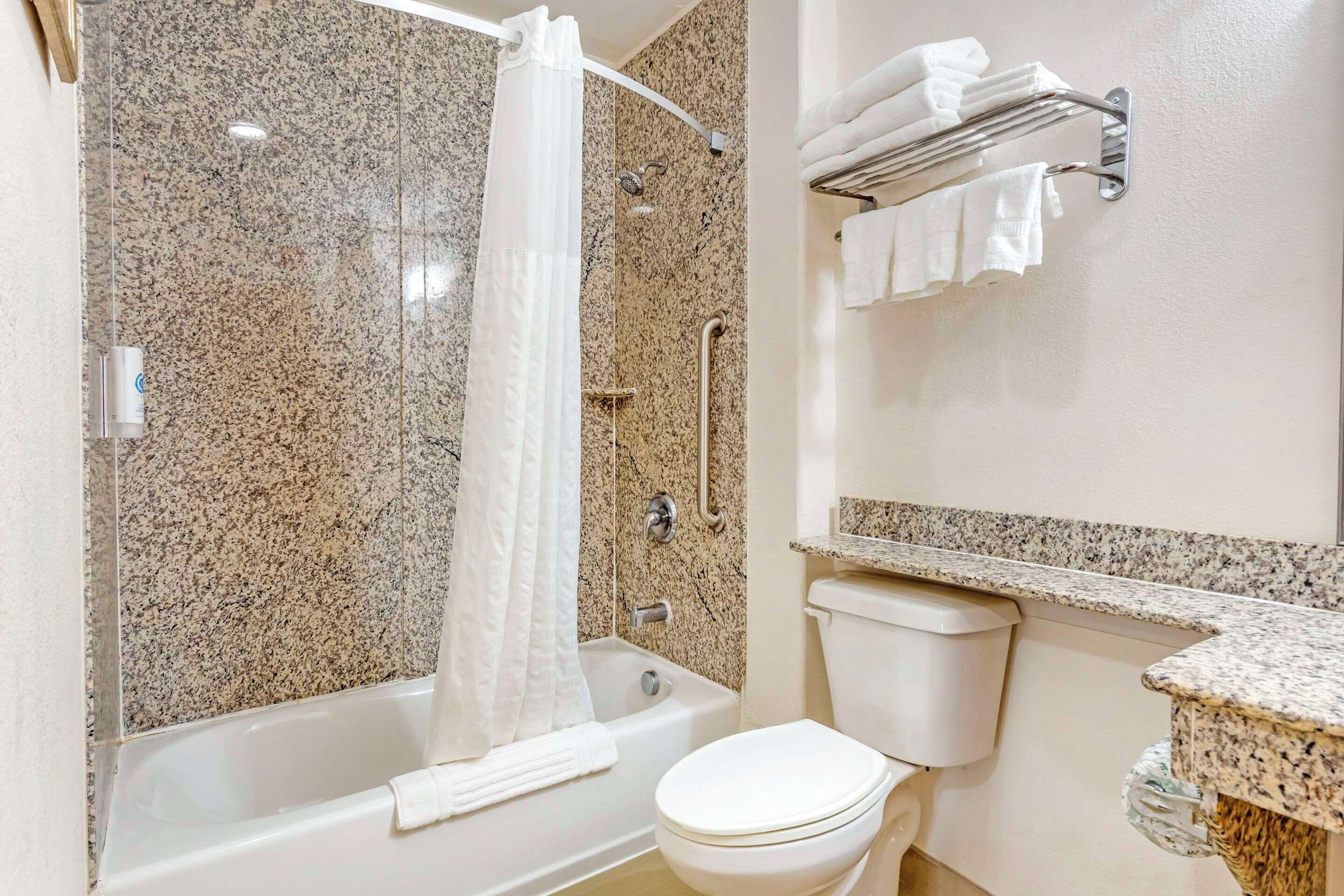 A bathroom with a granite-tiled shower, a white toilet, and a towel rack with towels.